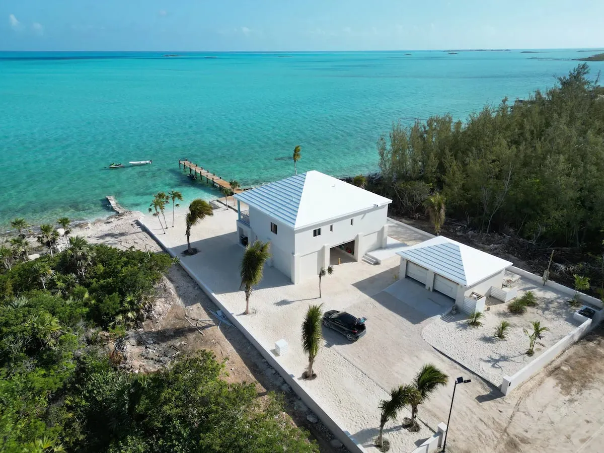 Aerial of the white beach house, garage, and private dock on turquoise water