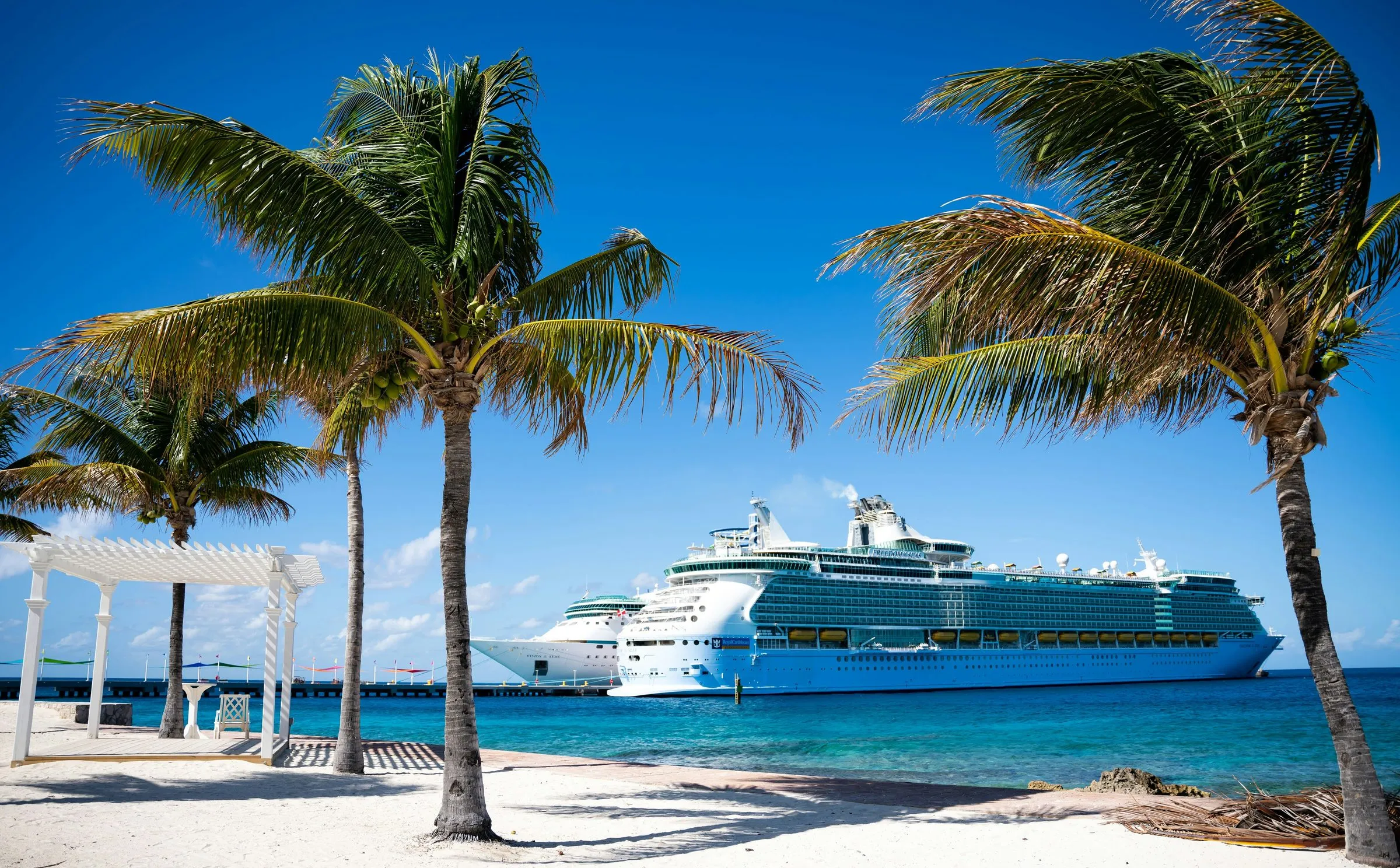 Cruise ships docked off a palm-lined Bahamian beach