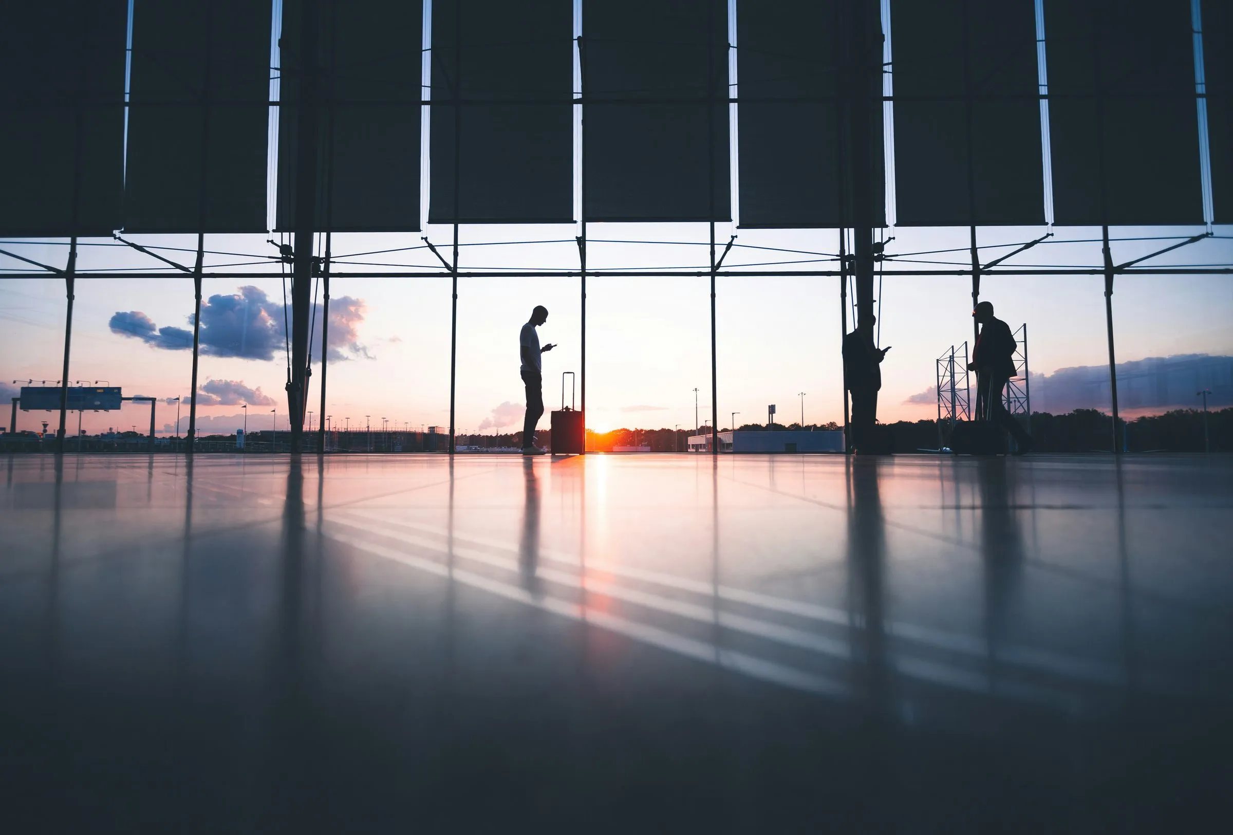 Travelers with suitcases silhouetted in an airport terminal at sunset