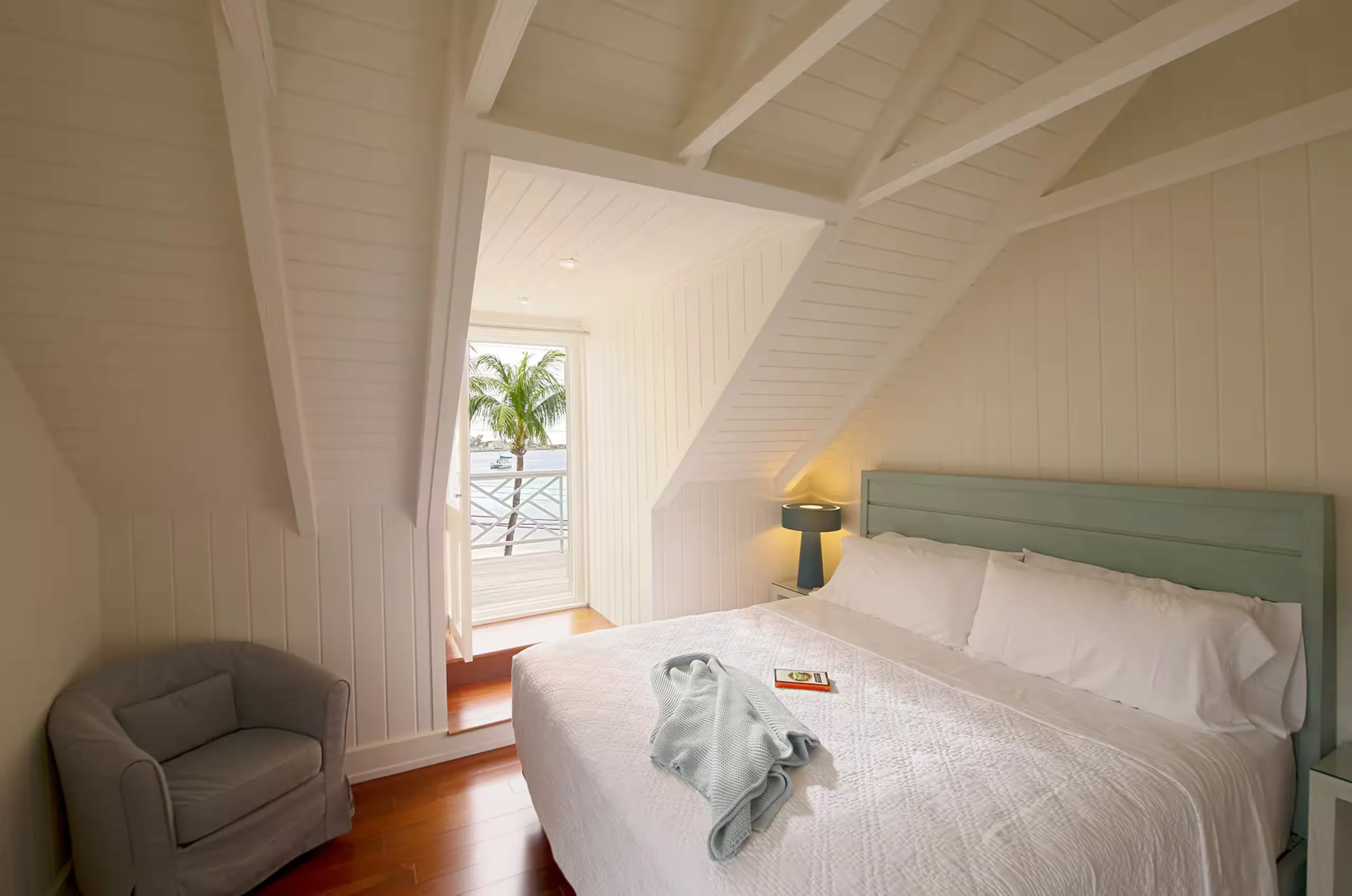 Bedroom under sloped ceilings opening onto a harbor-view balcony