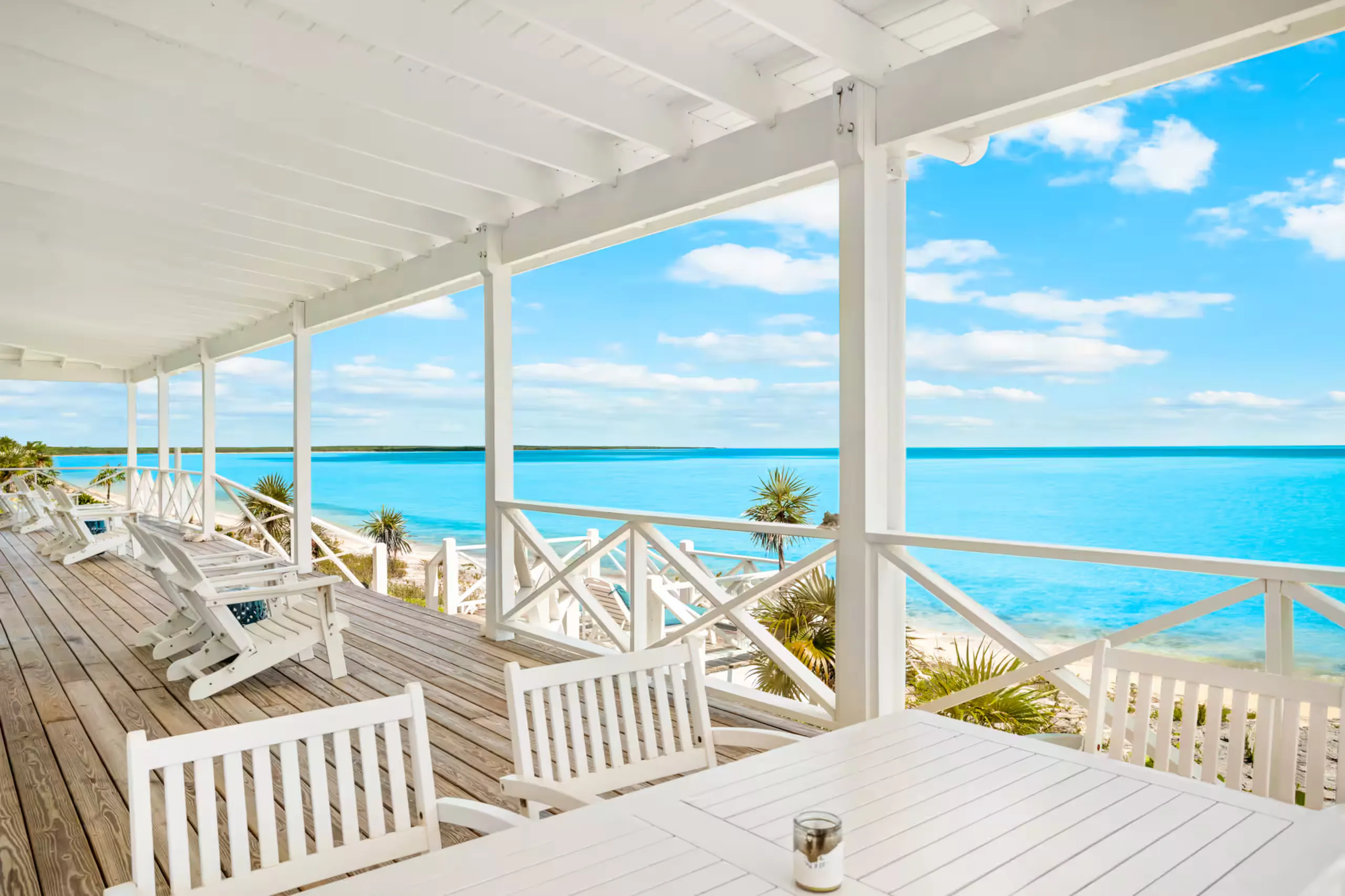 Covered deck with lounge chairs and a dining table facing the water