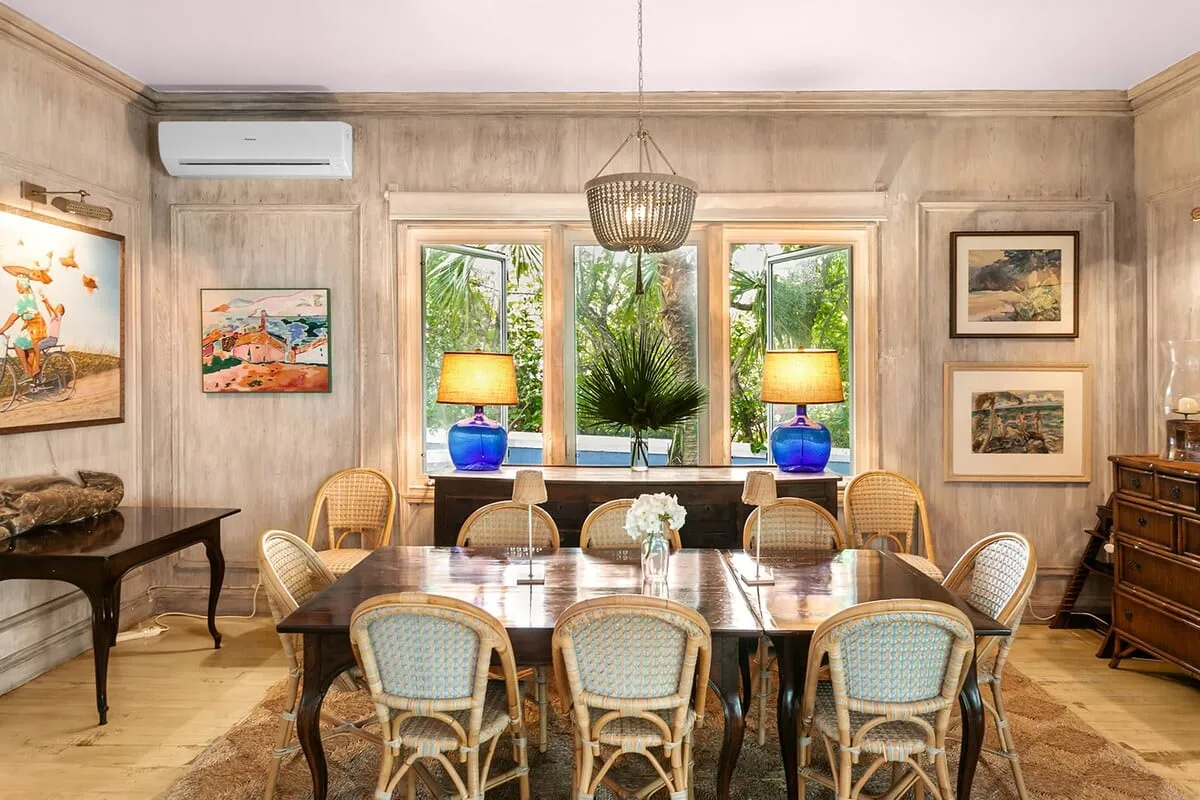 Dining room with a long wood table and windows onto tropical greenery