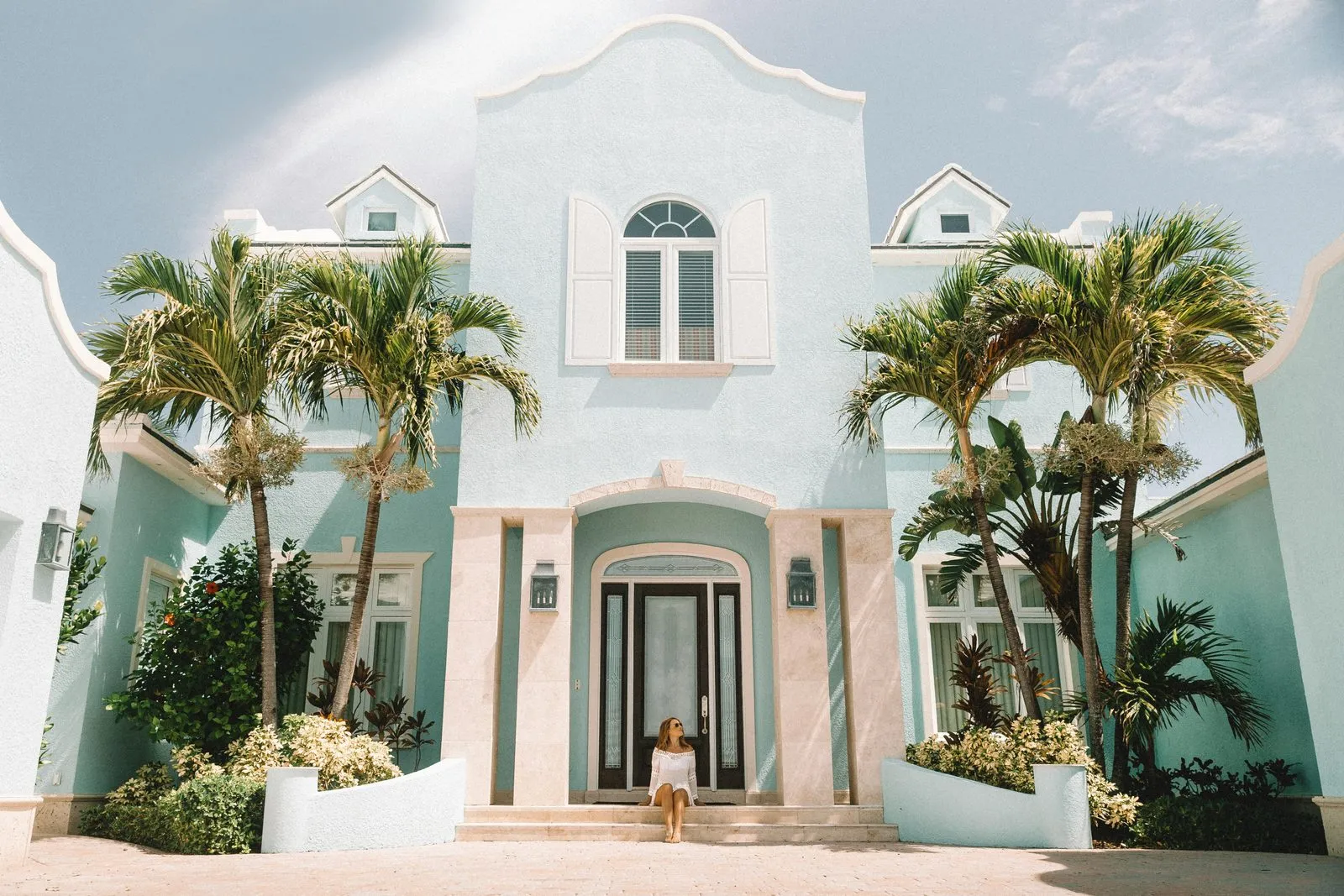 A pastel-blue colonial-style rental house behind palm trees in Exuma