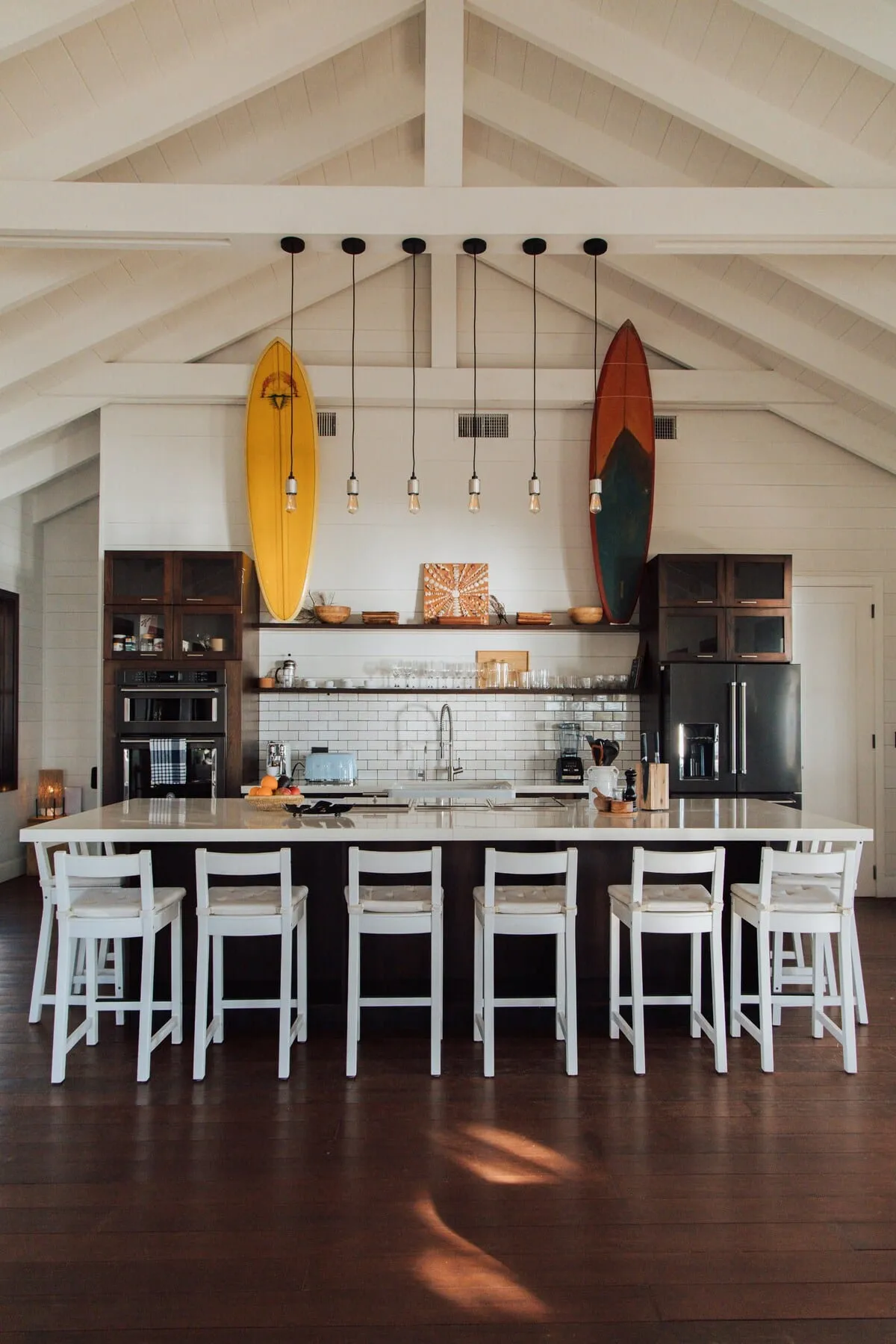 Kitchen island with bar stools, dark wood cabinets, and surfboards on the wall