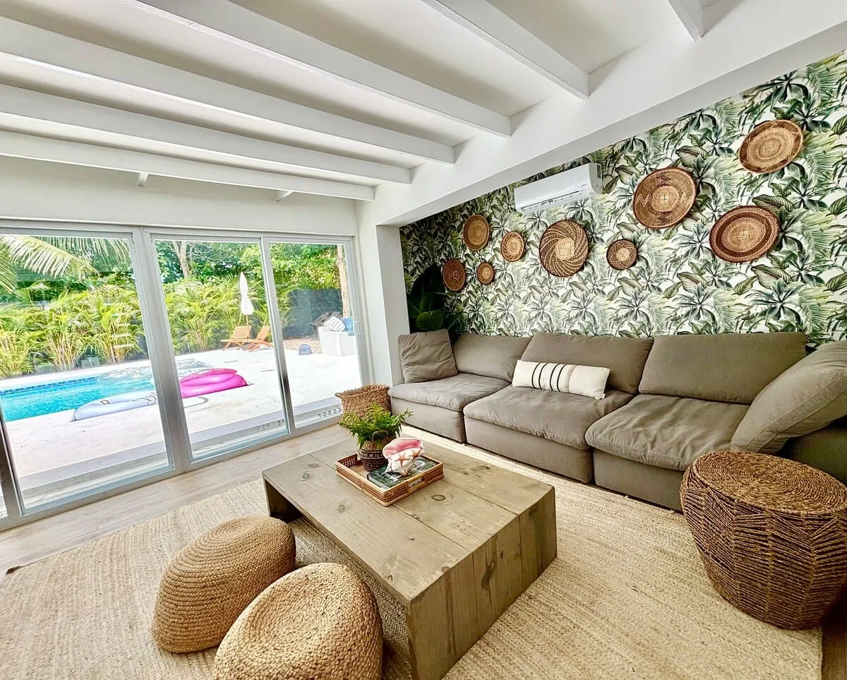 Sectional facing a tropical accent wall with woven baskets and pool doors beyond