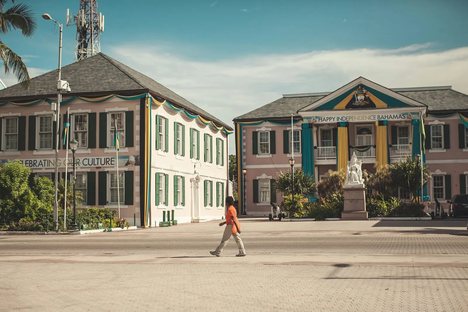Parliament Square in downtown Nassau, colonial pink-and-white government buildings decorated for Independence Day, with a pedestrian crossing the plaza