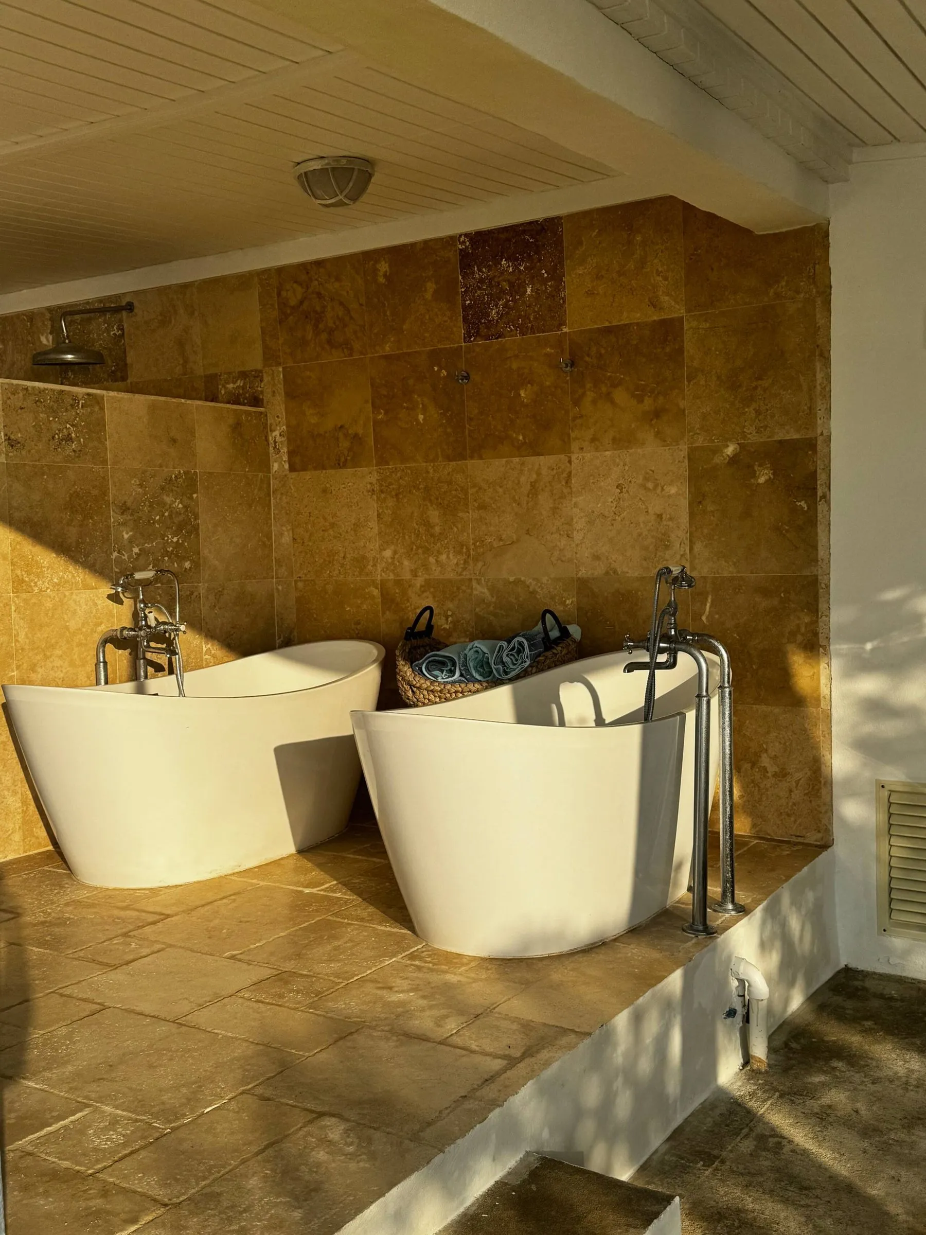 Two freestanding outdoor bathtubs on a tiled patio