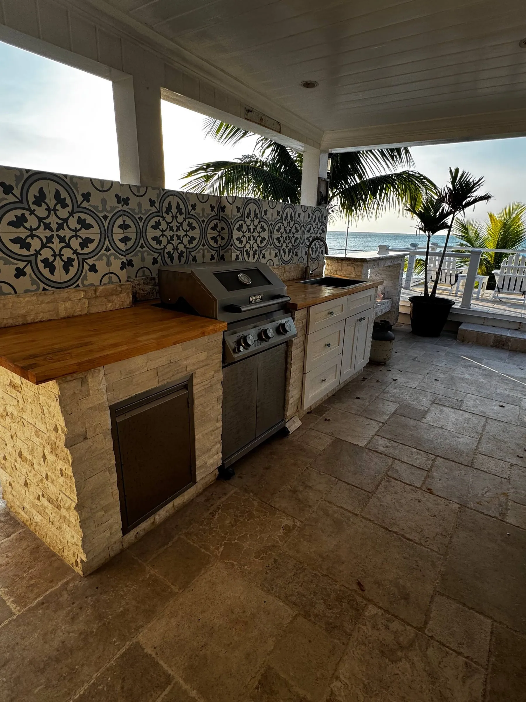 Outdoor kitchen with a grill and tiled backsplash facing the ocean