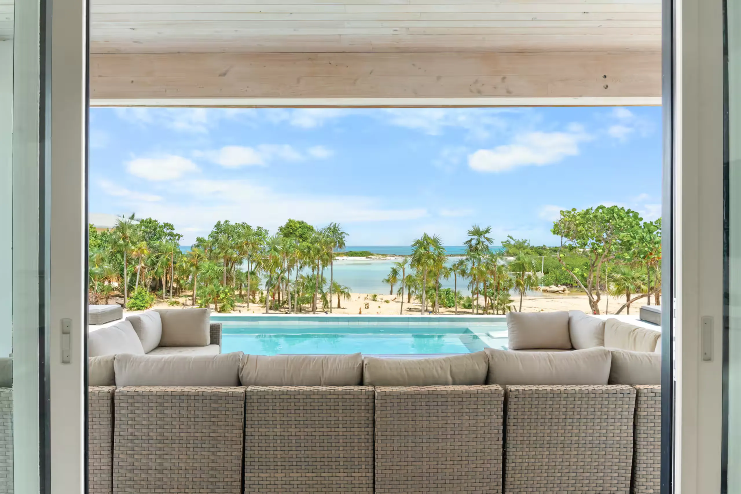 Covered patio sofa facing the pool with ocean visible through the palms