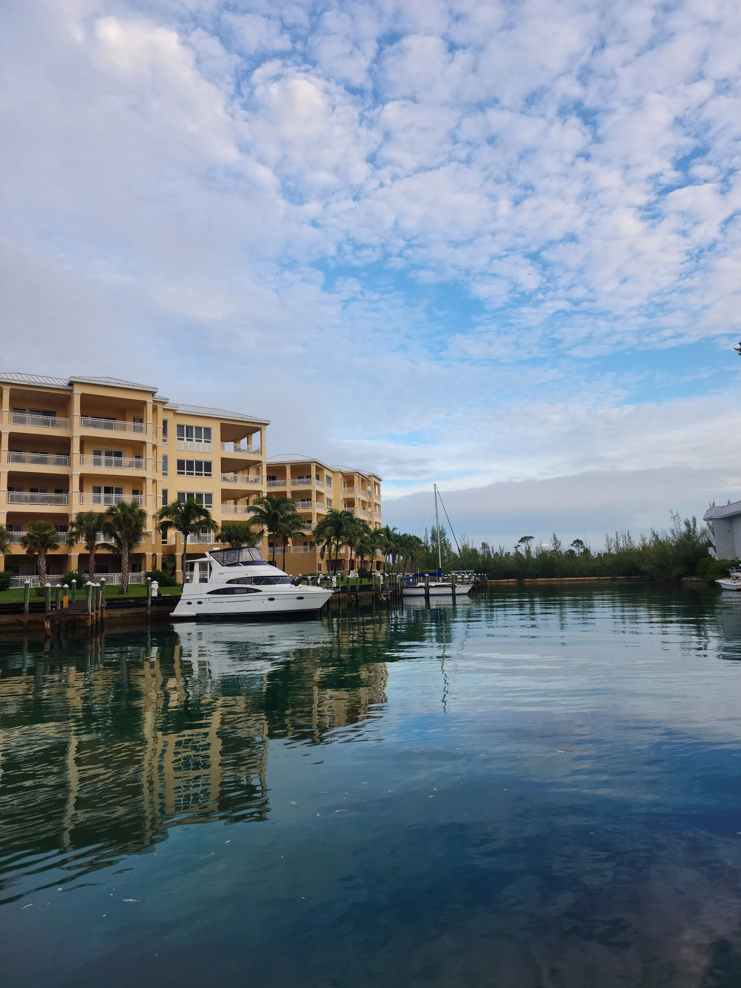 Pastel condos and palm trees along a still marina canal in Grand Bahama, with a yacht and sailboat moored at the dock