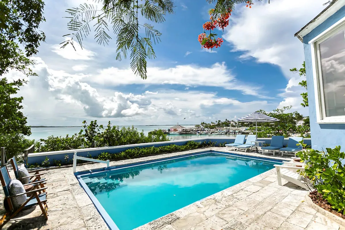 Pool deck with lounge chairs and blue-striped umbrellas overlooking the harbour