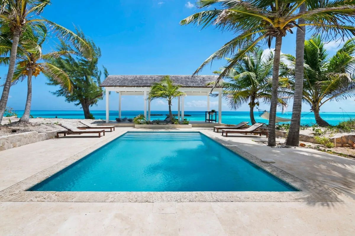 Pool and white pavilion looking out to turquoise ocean through palms