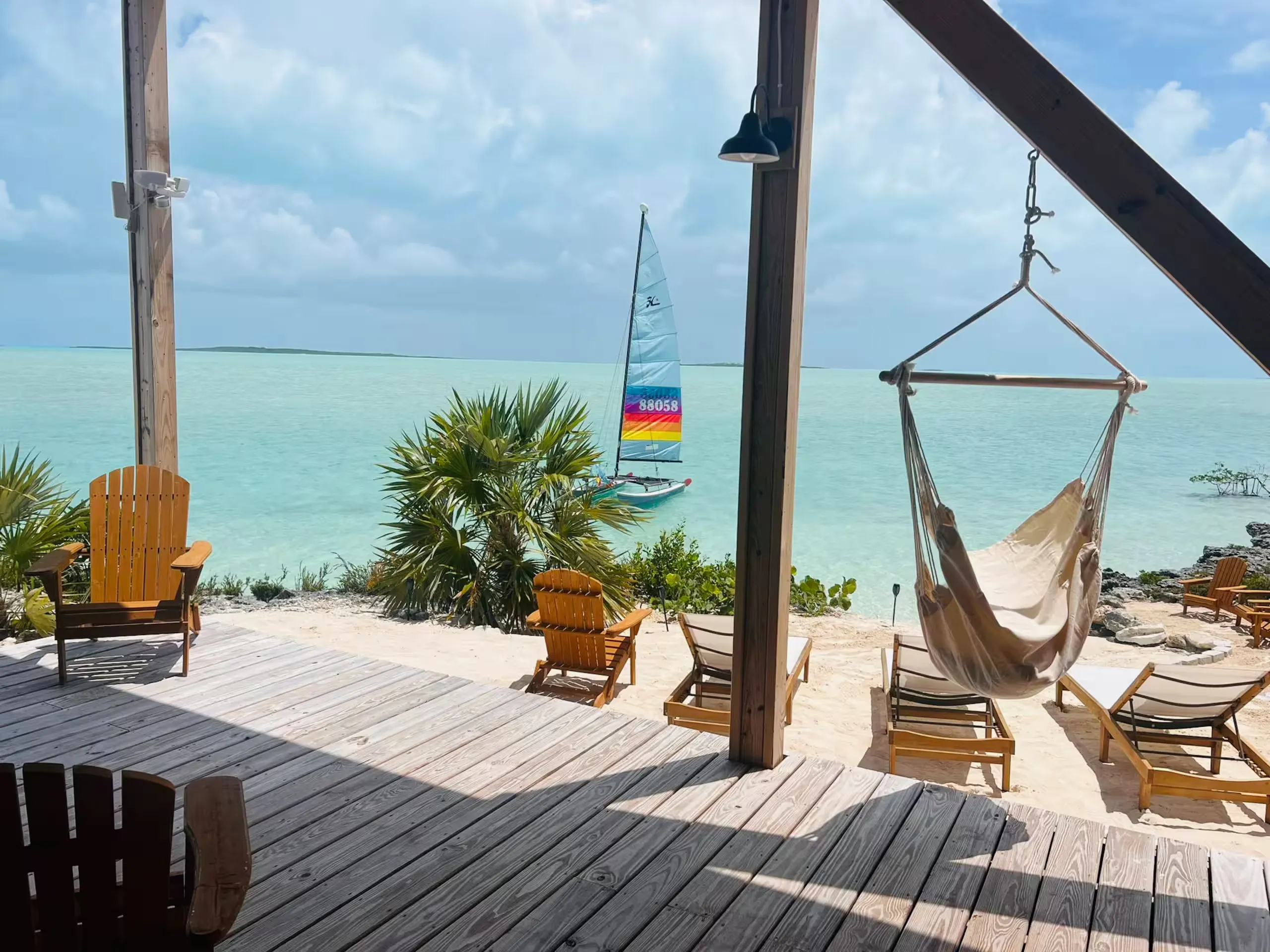 Covered porch with a hanging hammock chair and a catamaran offshore