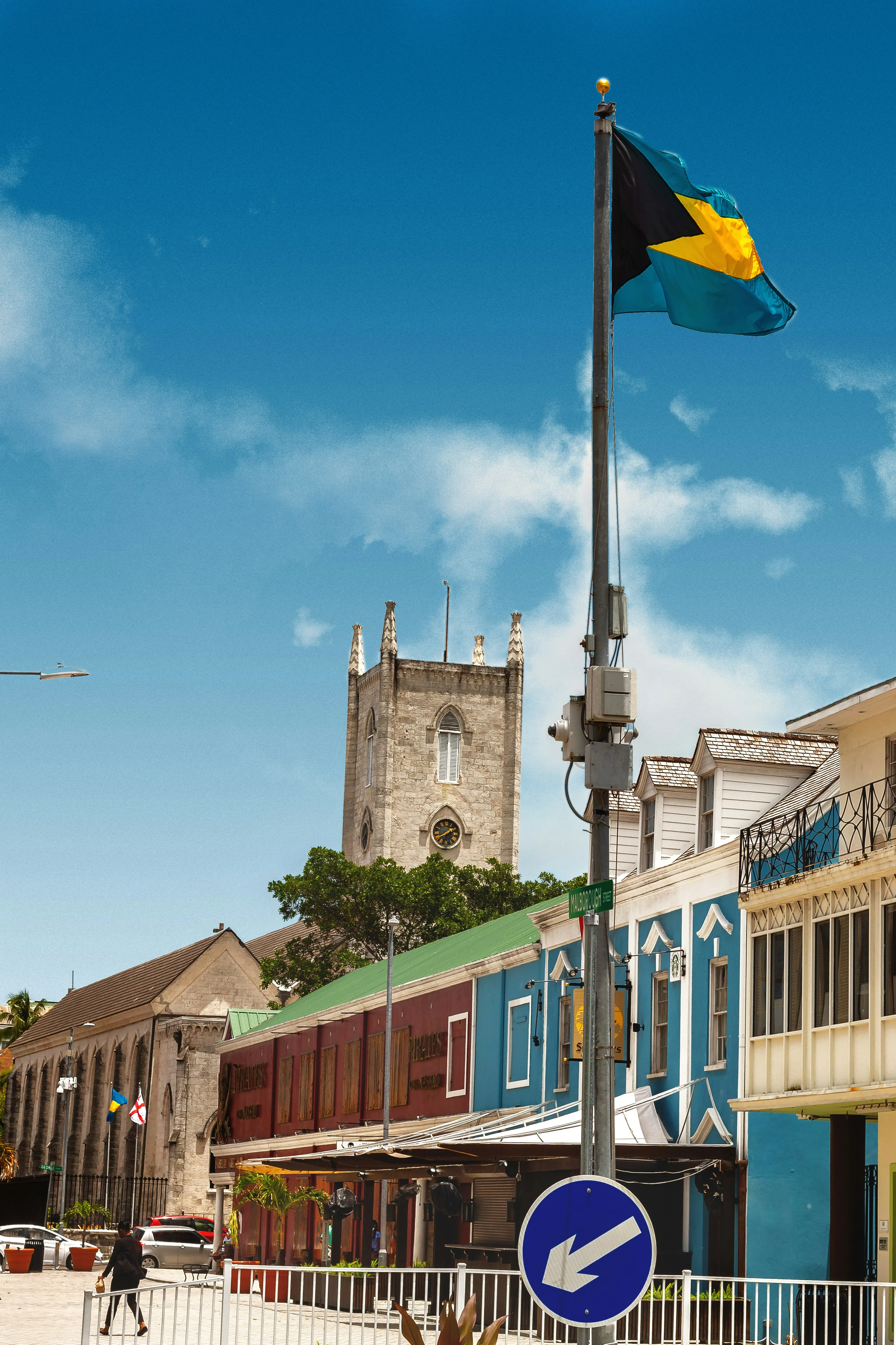The Bahamian flag flying over a colorful Nassau street, with a historic clock tower behind